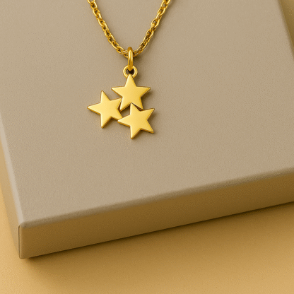 Collier doré en acier inoxydable avec pendentif trois étoiles posé sur une boîte grise