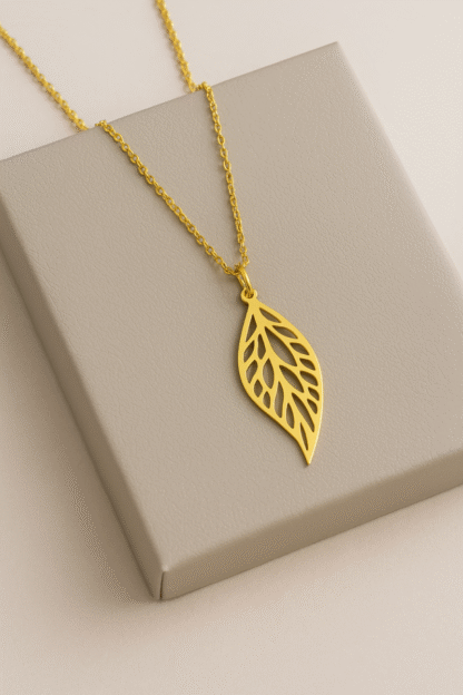 Collier pendentif feuille doré en acier inoxydable posé sur boîte grise