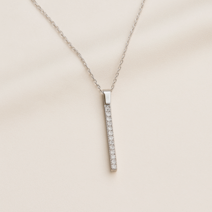 Collier en argent 925 avec pendentif barre serti de zircons, posé sur tissu beige clair