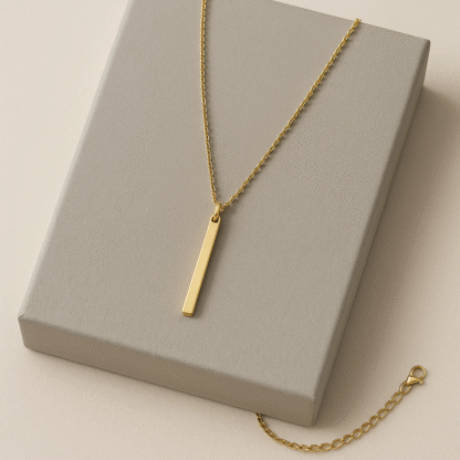 Collier doré à barre verticale en acier inoxydable posé sur boîte cadeau grise
