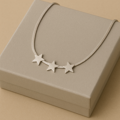 Collier doré maille plate avec étoiles posé sur une boîte cadeau gris clair